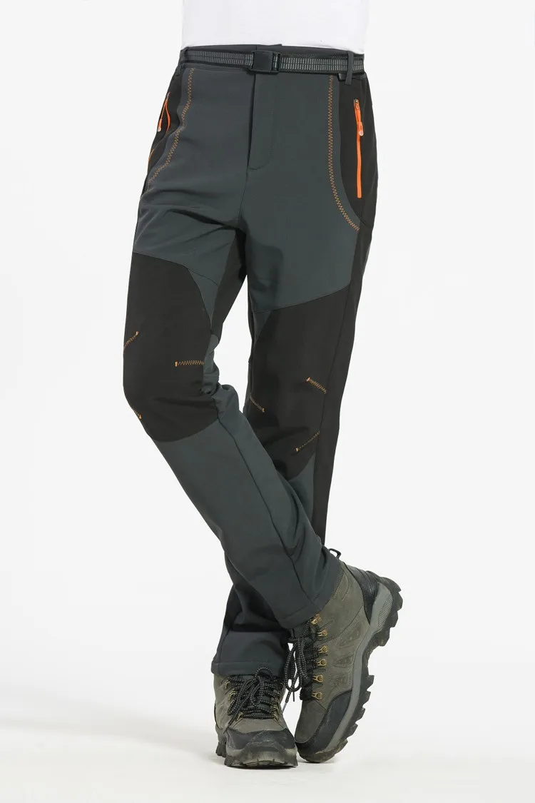 tumedad matkapüksid oranžide detailidega, jalas matkajal