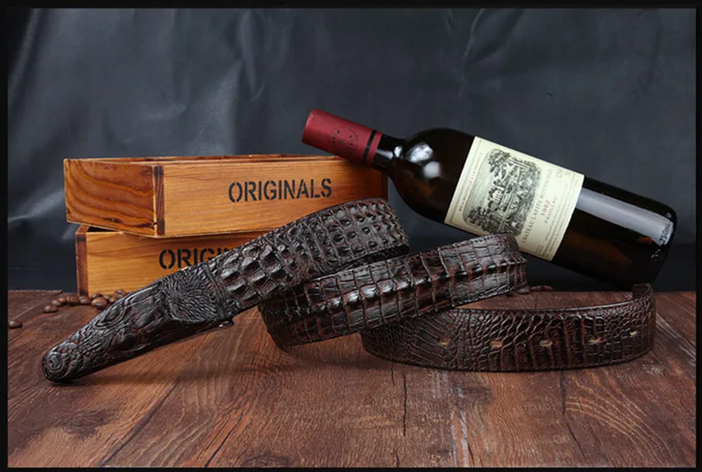 kolm krokodillinaha mustriga pruuni nahast püksirihma puidust kastide ja veinipudeli taustal