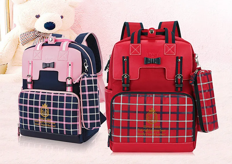 kaks ruudulise mustriga koolikotti, üks punane ja teine roosa, mõlemal ees taskud ja sangad