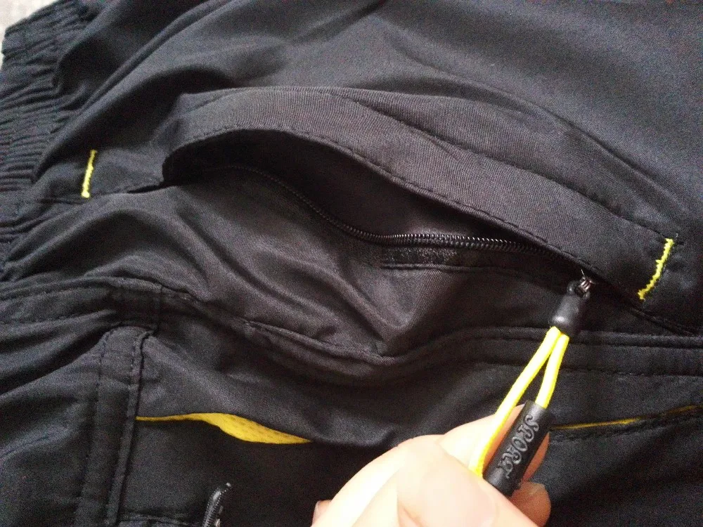 mustad meeste püksid kollaste detailidega ja lukuga tasku