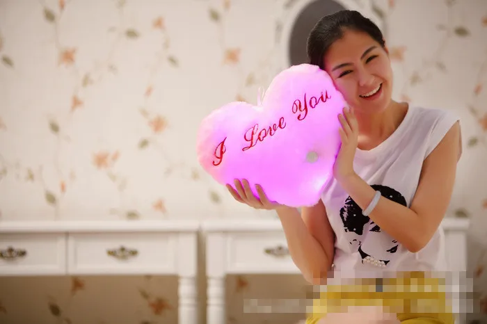 naeratav naine hoiab südamekujulist LED padja, millel on kiri 'I Love You'