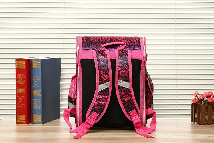 roosa ja musta mustriga koolikott laual, taustal raamatud ja lilled